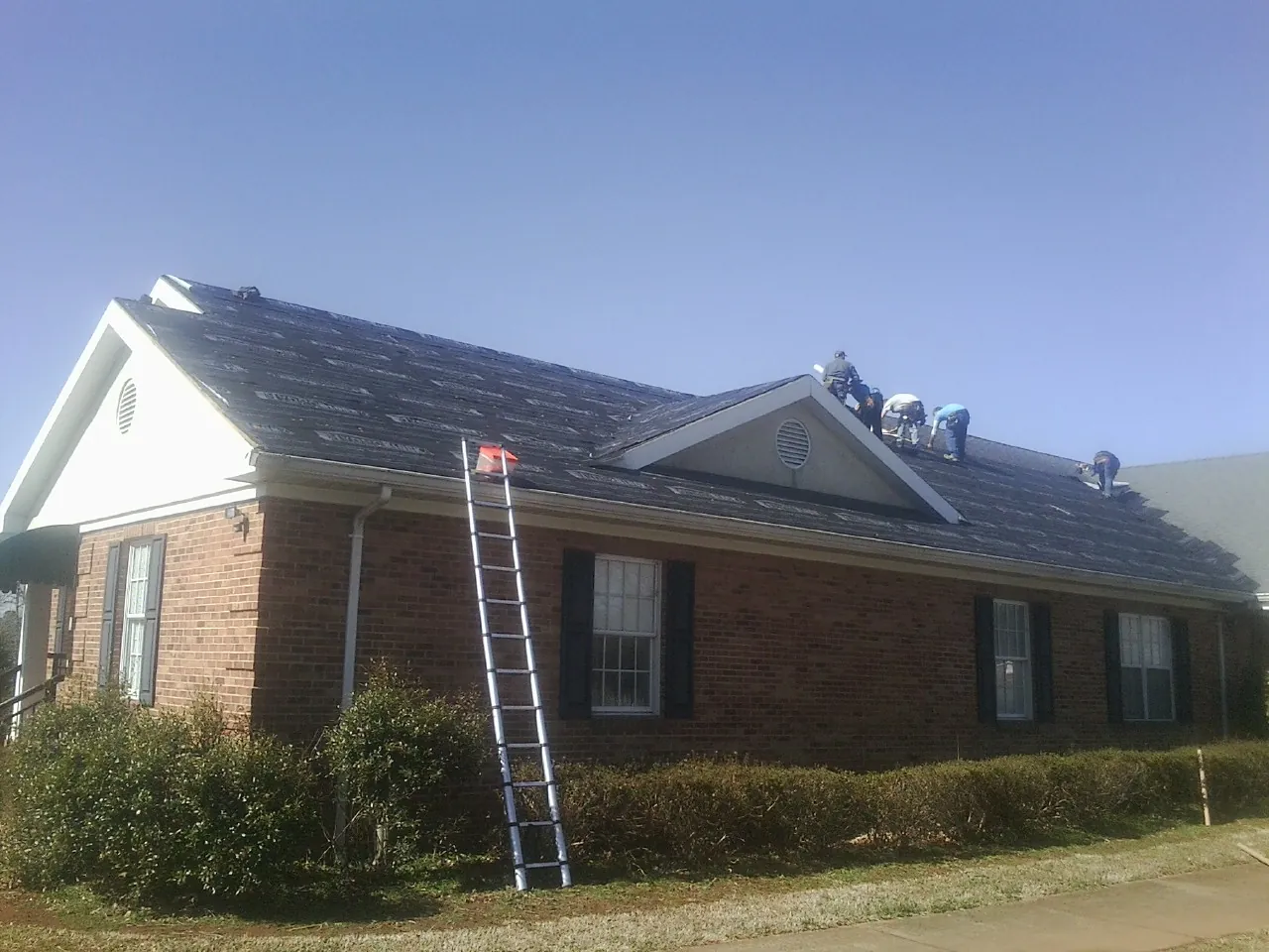 Crew tearing shingles off a brick ranch roof with a ladder set — Emergency Roof Repair work by our crew in Weimar