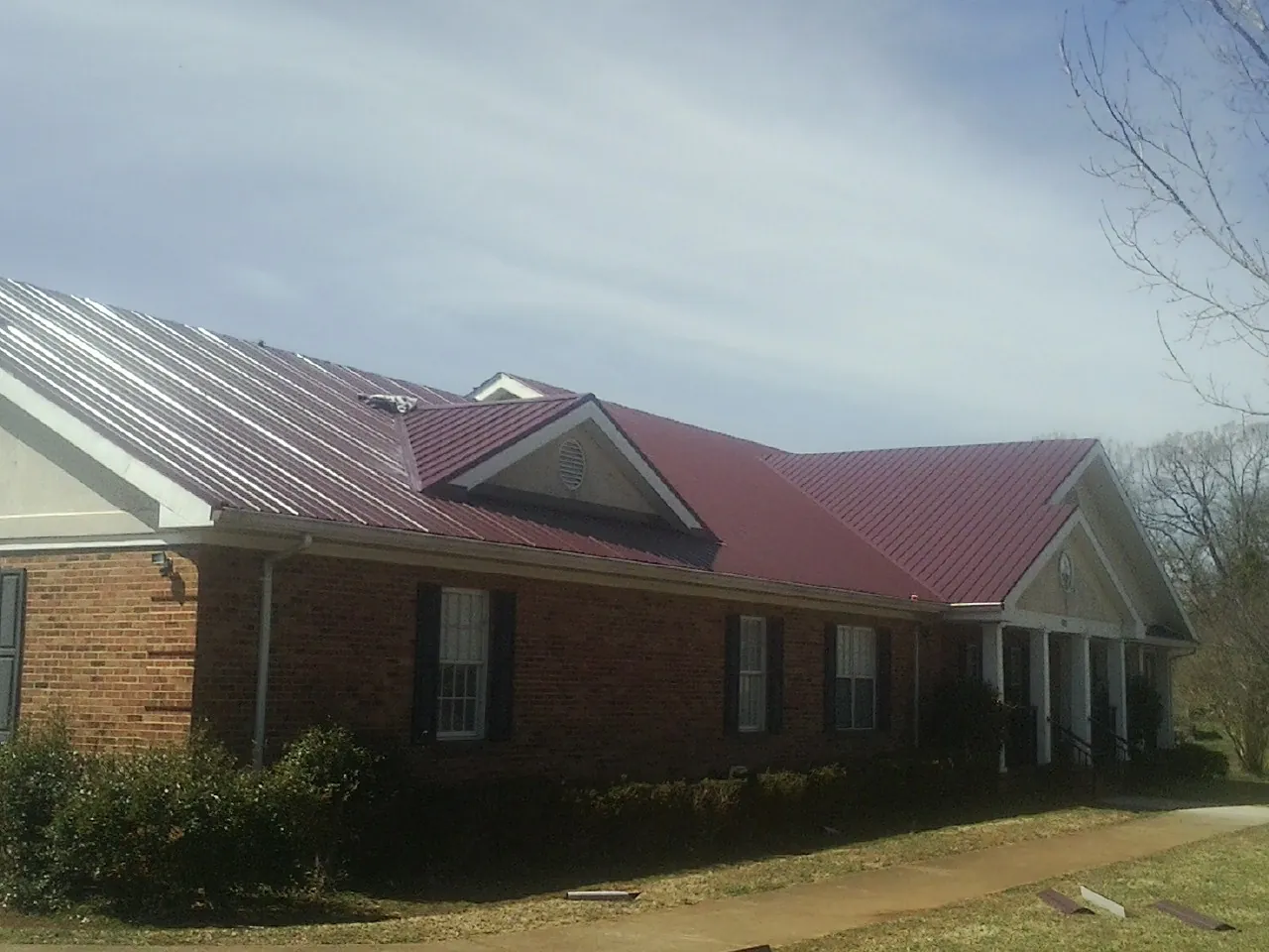 Red metal roof with gabled entries on a long brick building, from a Hail Damage Roof Repair job in Weimar