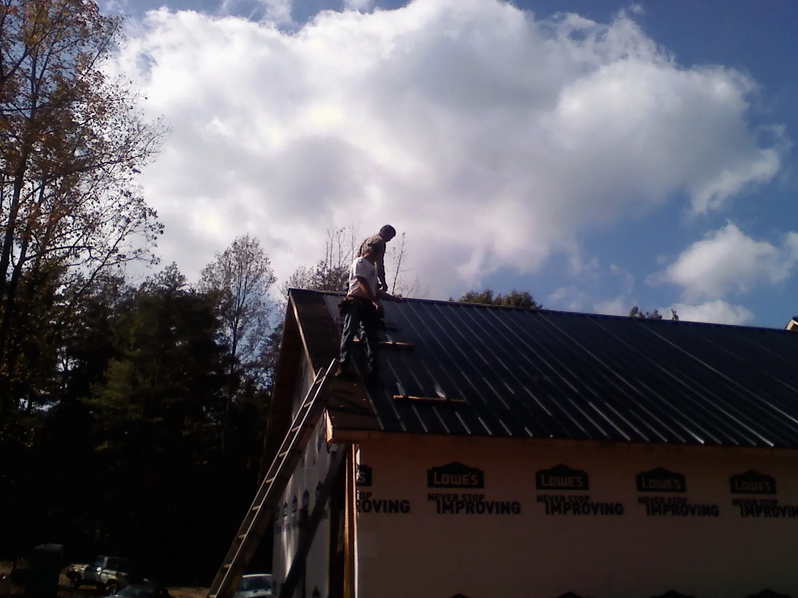 Roofer fastening dark metal panels high against a cloudy sky, from a Roof Inspection job in Weimar