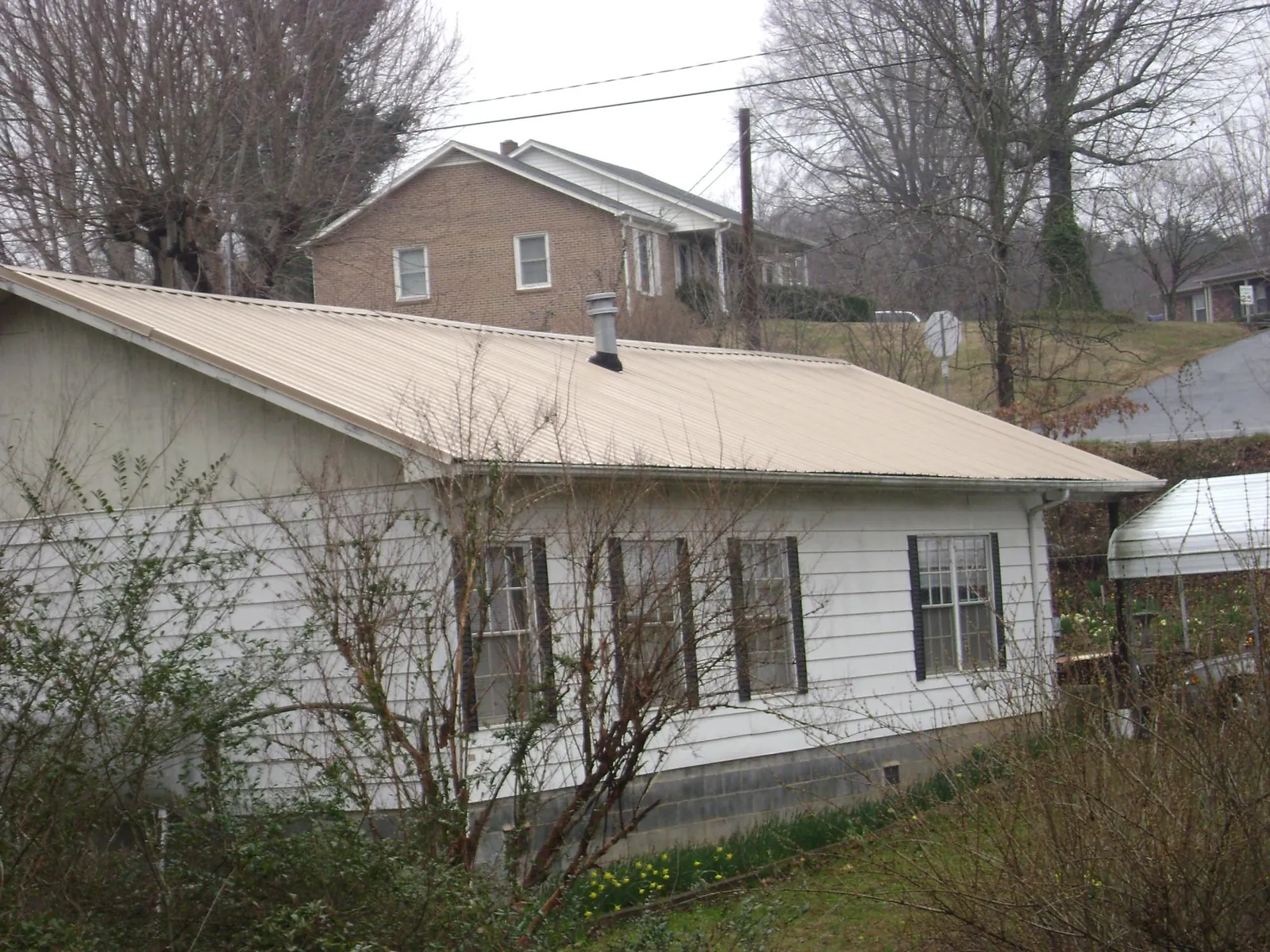 Tan metal roof on a white sided house set into a hillside — Commercial Roofing by Roofing Brothers in Weimar