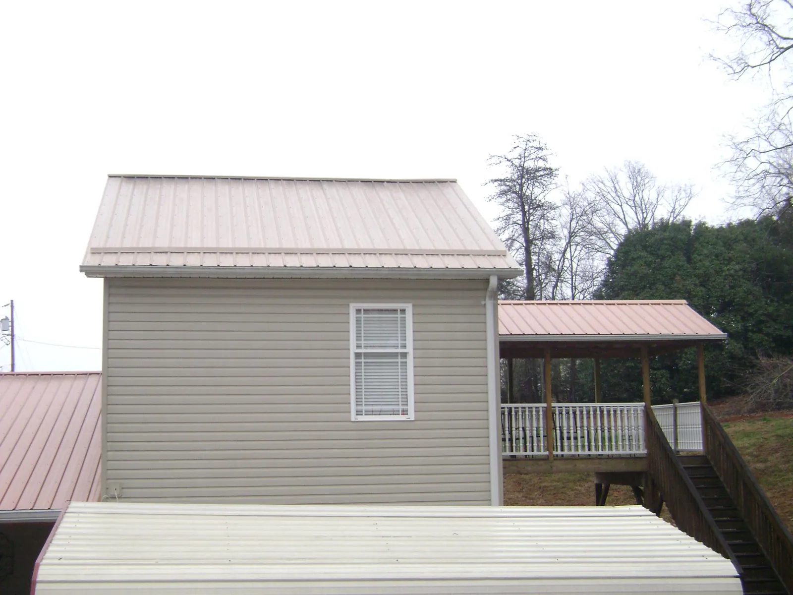 Tan metal roofs on a two story addition and attached porch, from a Roof Replacement job in Weimar